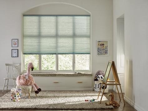 Honeycomb cellular shades in a soft blue-green fabric over a window seat in a child's room