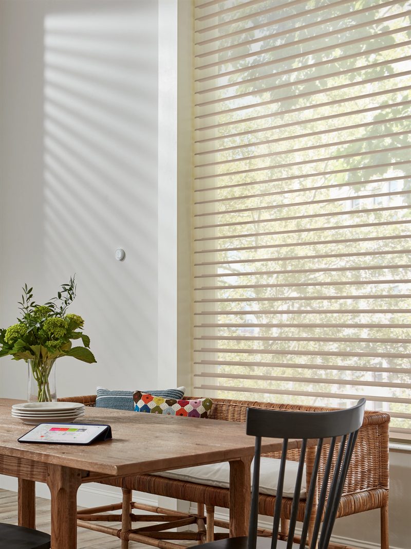 Nantucket sheer shades softening the light over a tall window beside a wooden dining table