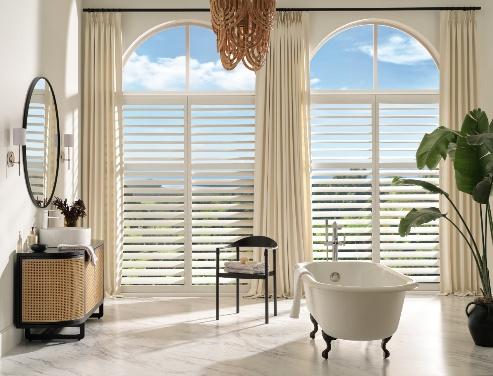 White plantation shutters over arched windows in a spa-style bathroom