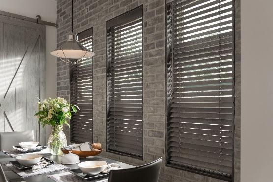 Dark wood blinds over three tall windows in a dining room with exposed brick